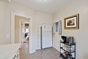 Cozy retreat with a white bed, wardrobe, and refrigerator, perfect for a functional stay.