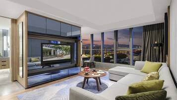 A modern living room with a large TV, a sofa, a coffee table, and a city view.