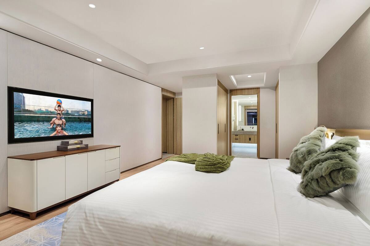 Une chambre d’hôtel moderne dotée d’un grand lit, d’un téléviseur à écran plat fixé au mur, d’une armoire en bois et offrant une vue sur la ville par la fenêtre.