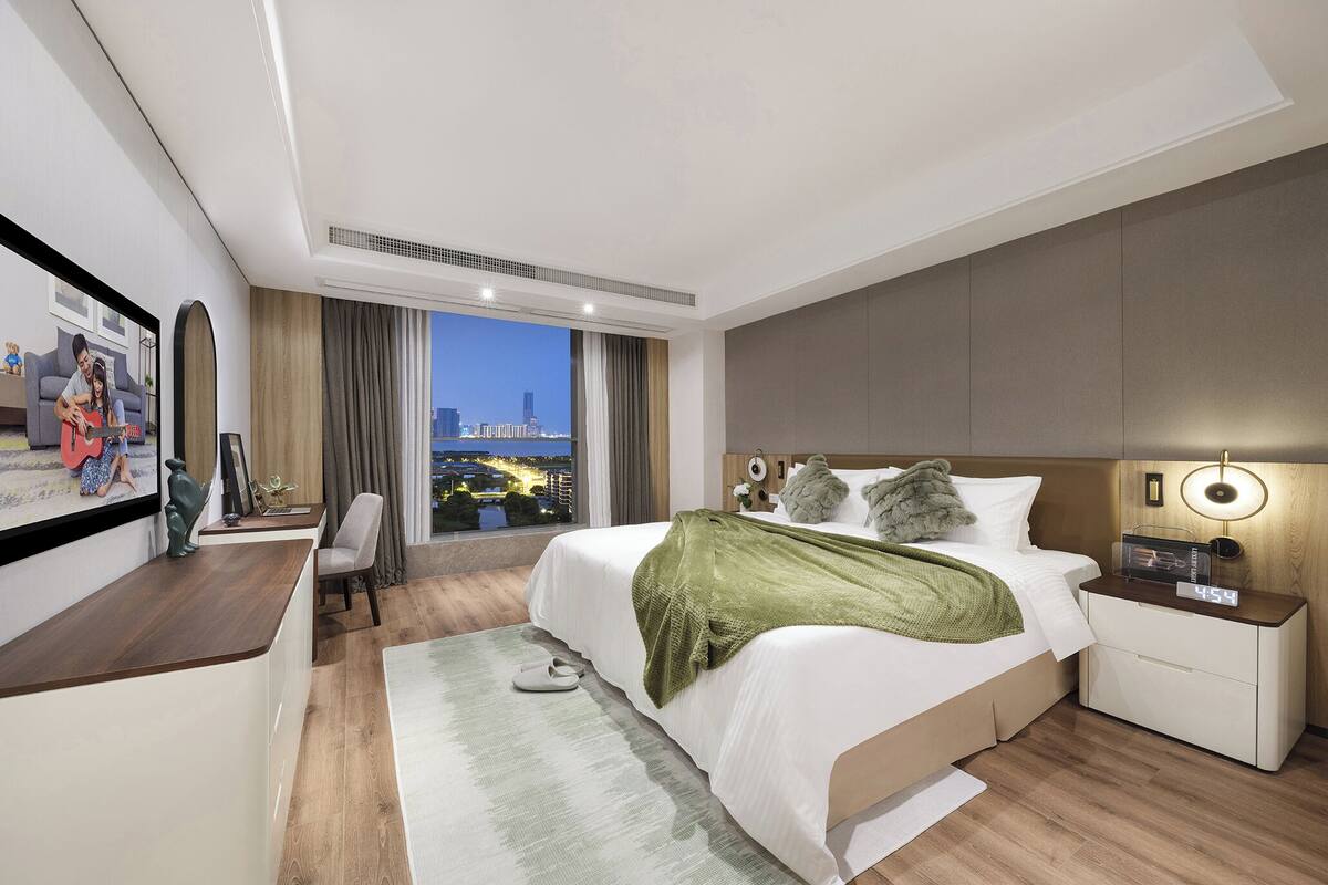 Une chambre d’hôtel moderne, dotée d’un grand lit, d’un bureau, d’une télévision et offrant une vue sur le paysage urbain.