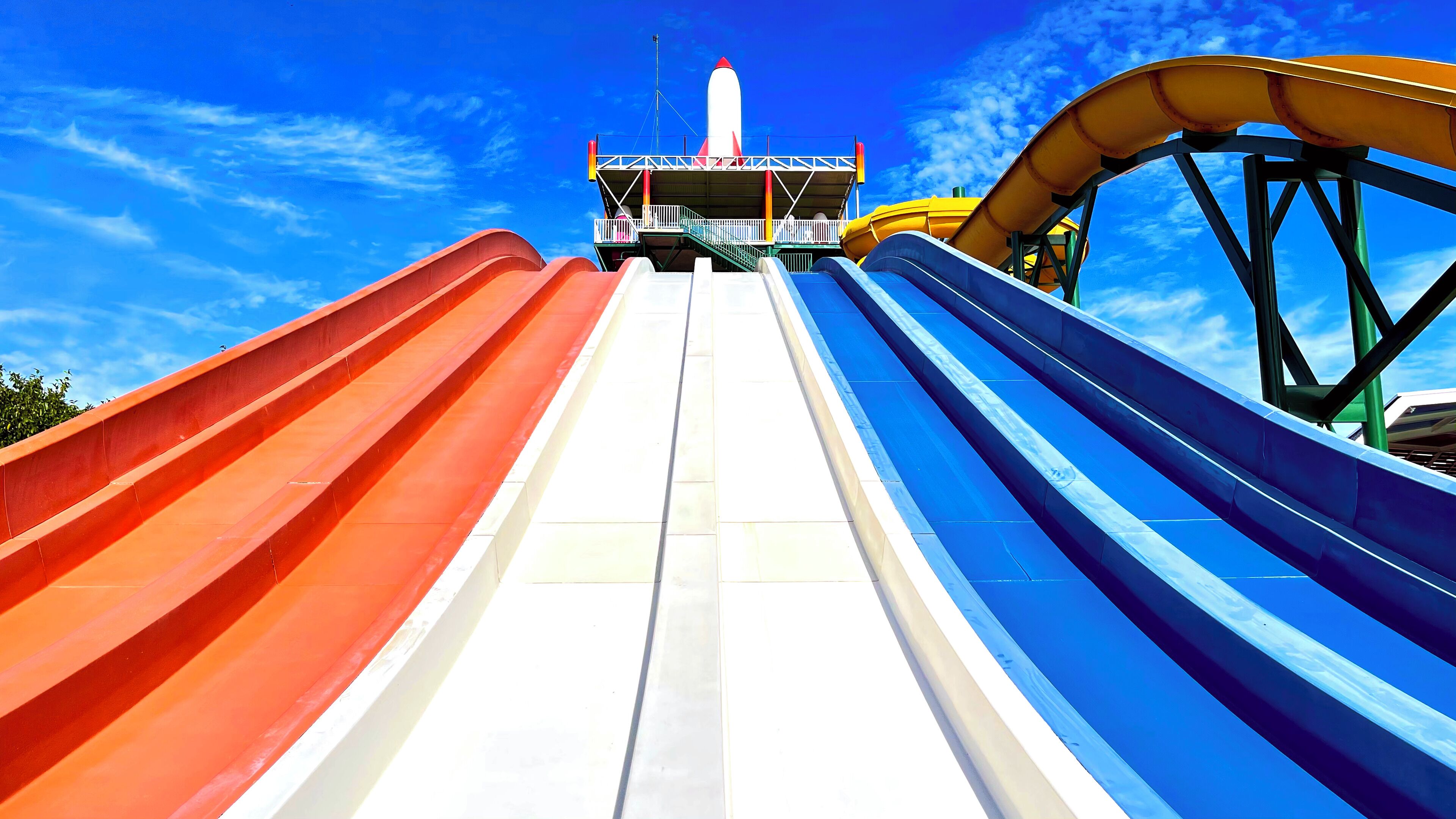 Een waterglijbaan met meerdere banen, een startplatform en een helderblauwe lucht op de achtergrond.
