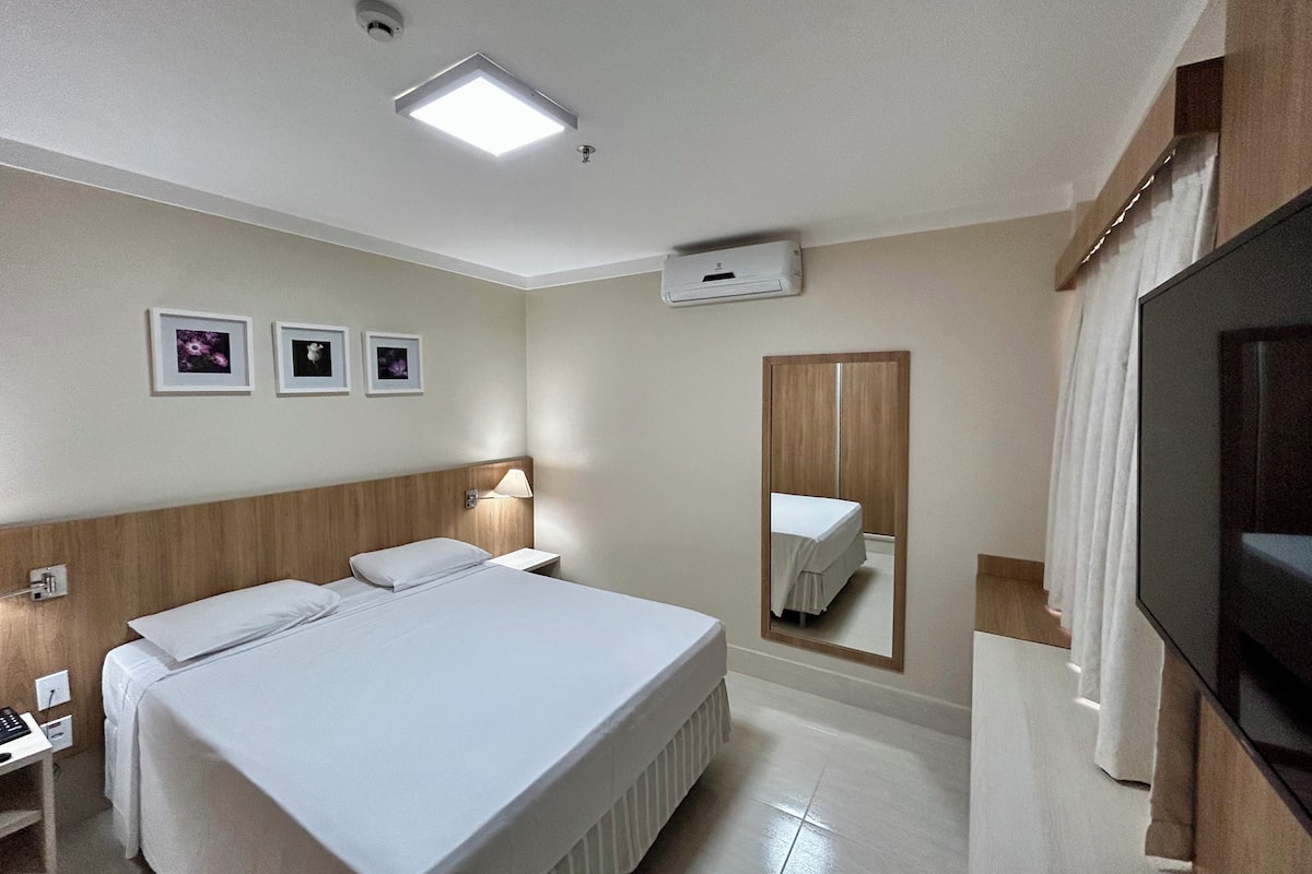 Une chambre d’hôtel avec un lit, une table de chevet, une lampe, un miroir et un téléviseur.