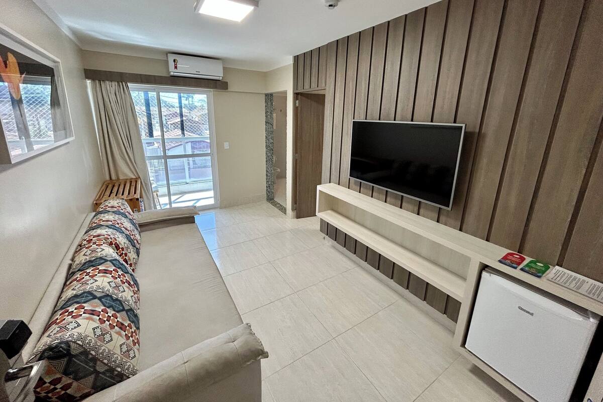 Un salon moderne avec un téléviseur à écran plat fixé à un mur en bois, un canapé agrémenté de coussins à motifs, une petite table et un mini-réfrigérateur.