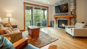 A spacious living room with a stone fireplace, comfortable seating, and a large window offering a view of the outdoors. - Great Location Near Pool with Suncadia Pool Access (Cle Elum)