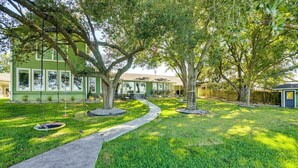 A green building with a covered outdoor seating area, surrounded by trees and a paved walkway. - Family Friendly Lakefront Luxury, Private Water trampoline, arcade, BYOB boat (Livingston)