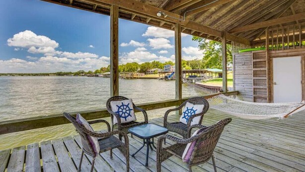 A wooden deck with wicker furniture and a hammock overlooking a body of water. - Family Friendly Lakefront Luxury, Private Water trampoline, arcade, BYOB boat (Livingston)