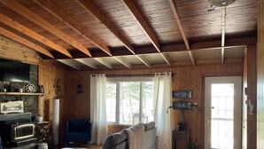 Interior acogedor de una cabaña con chimenea, un sofá, un comedor y un ventanal con cortinas.