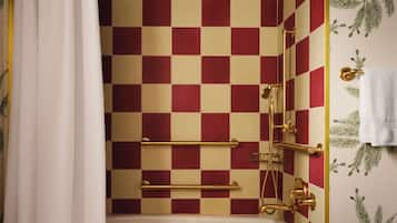Un baño con piso a cuadros rojo y beige, una bañera blanca y una ducha con detalles dorados.