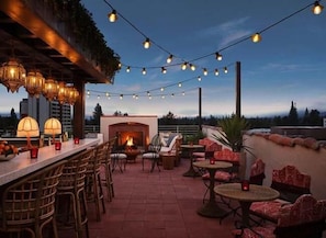 An outdoor patio with a brick fireplace, string lights, wicker furniture, and a view of the city skyline.