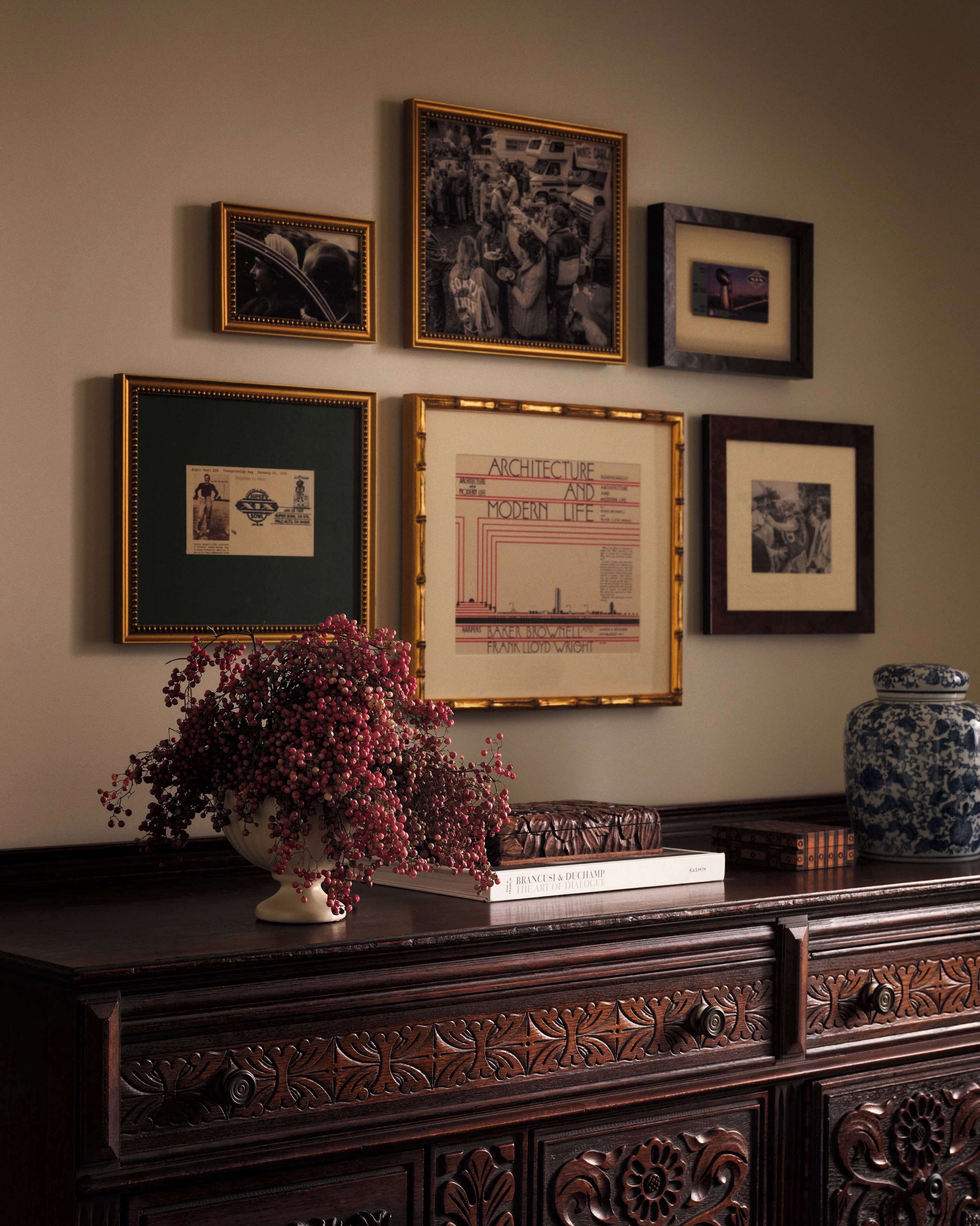 A wall with framed pictures and a vase with red berries.