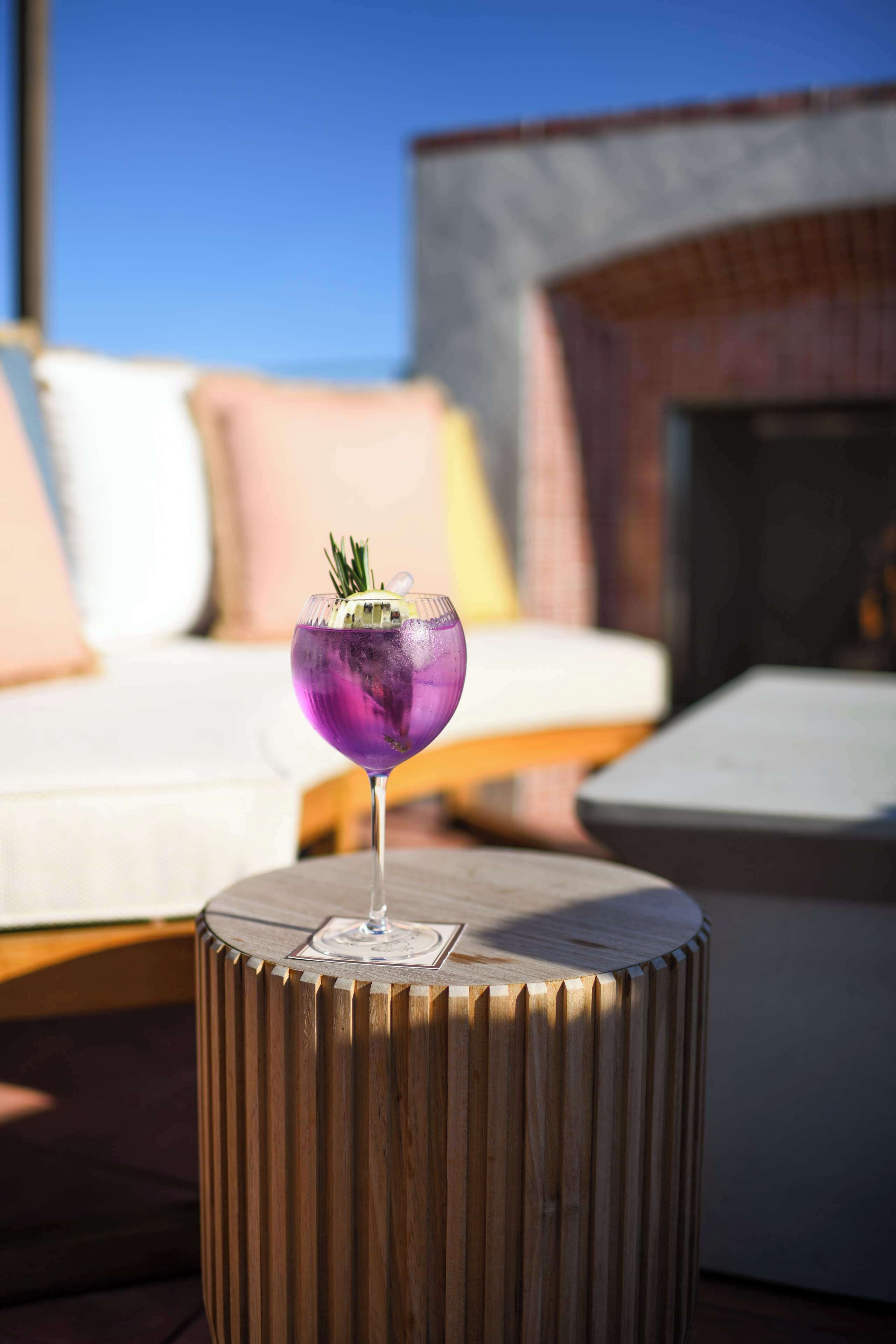 Ein Cocktailglas auf einem Holztisch mit Blick auf eine Lounge im Hintergrund.