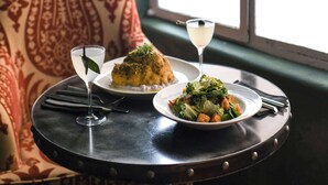 A dining table with a plate of food and a glass of water, set against a patterned chair and a window. - Graduate by Hilton Palo Alto (Palo Alto)