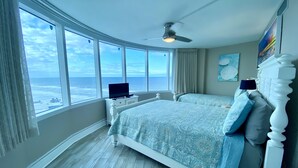 Une chambre avec une grande fenêtre, un ventilateur de plafond et un lit doté d’une tête de lit.