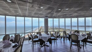 Un restaurant offrant une vue panoramique sur l’océan, avec de hauts plafonds et un mobilier moderne.