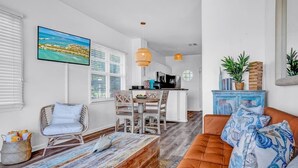 Un soggiorno moderno con un tavolino in legno, un divano con cuscini decorati, un'area pranzo con tavolo e sedie, e una cucina sullo sfondo.