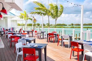 Un espace extérieur aménagé pour les repas, avec des tables et des chaises, donnant sur une étendue d’eau.
