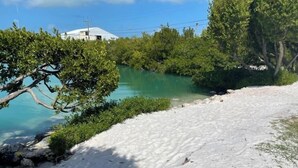 Una spiaggia sabbiosa con acque cristalline turchesi, circondata da una fitta vegetazione verde e un edificio bianco sullo sfondo.