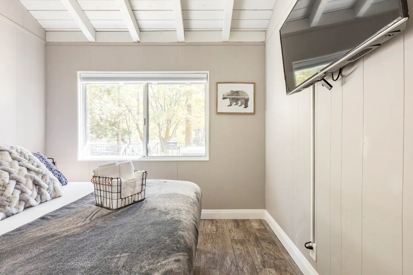 Un dormitorio con cama, ventana, televisión montada y un cuadro en la pared.