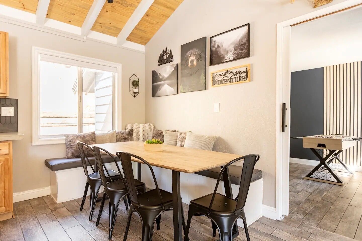 Een eetruimte met een houten tafel en zwarte stoelen, een bank met kussens en een wand met ingelijste foto's.