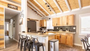 Une cuisine moderne avec des meubles en bois, un îlot central doté de tabourets de bar et un réfrigérateur en acier inoxydable.