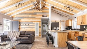 Un vaste espace de vie comprenant une cuisine moderne, des poutres apparentes en bois au plafond et un coin salon confortable.