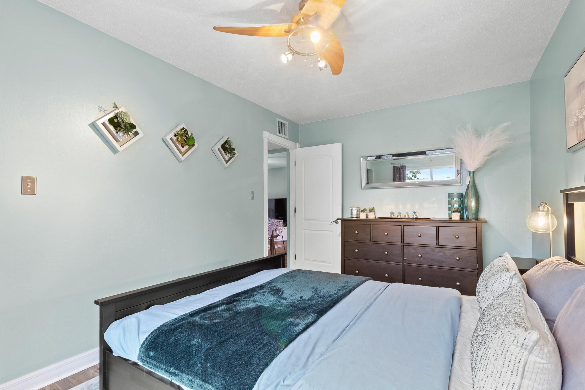Un dormitorio con cama, cómoda, ventilador de techo y adornos en la pared.