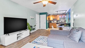 Un soggiorno moderno con una TV a schermo piatto, una ventola a soffitto e un divano grigio.