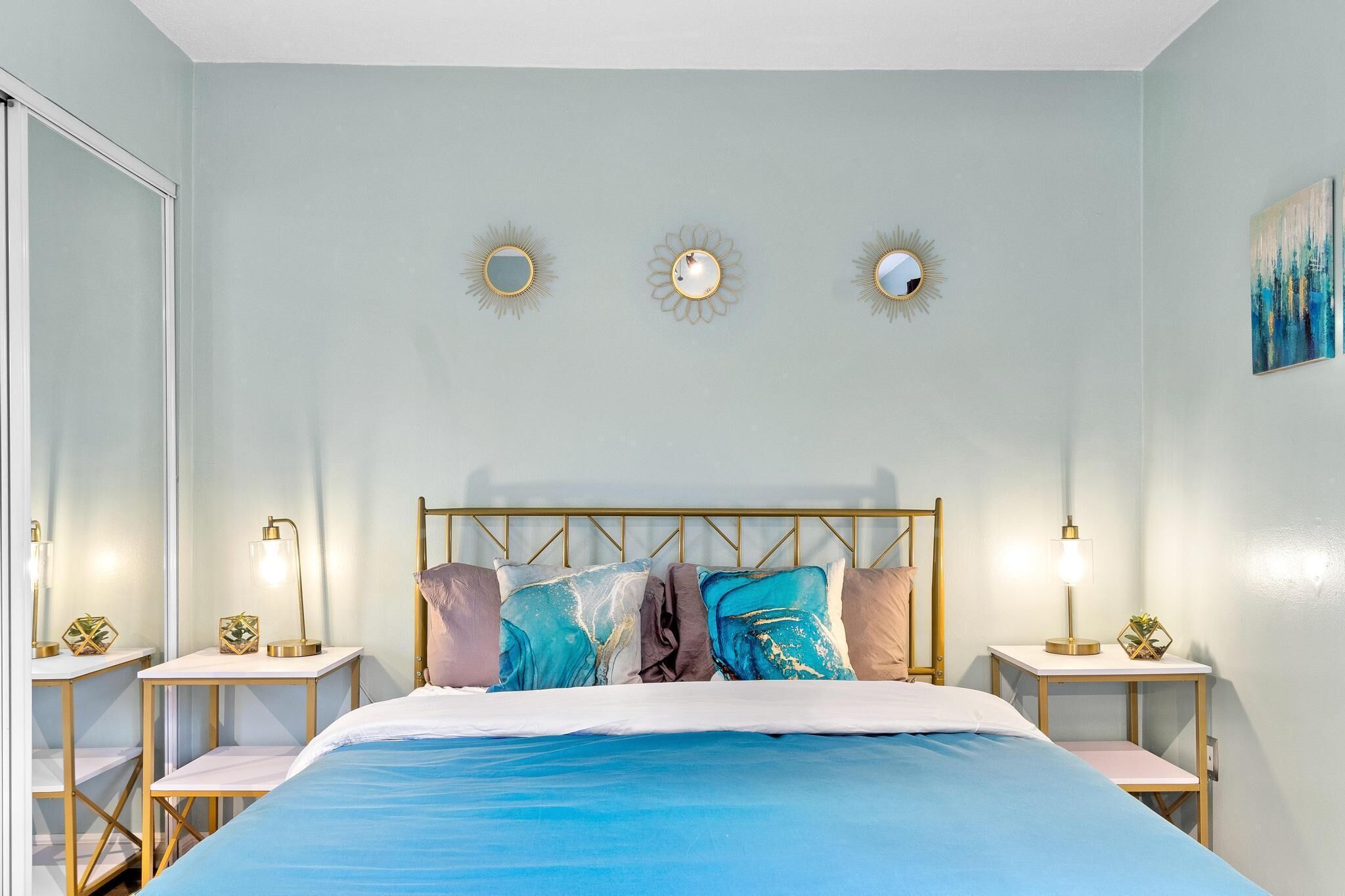 A bedroom with a bed, bedside tables, and wall-mounted mirrors.