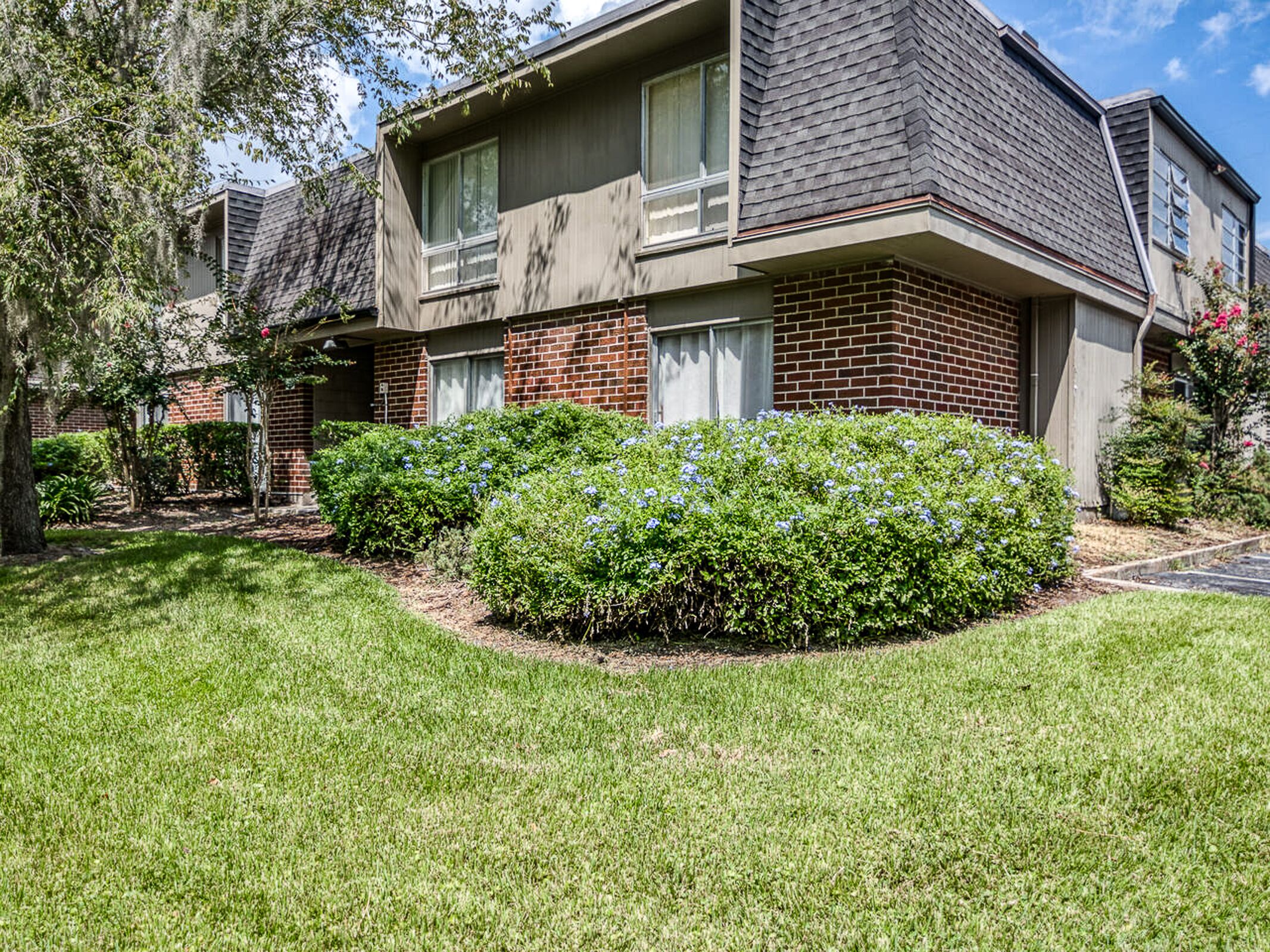 A two-story building with a brick facade and a small front yard with a well-maintained lawn and bushes.