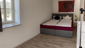 A bedroom with a bed, a window, a red artwork, and a wooden floor.
