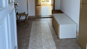 A room with a tiled floor, a bench, a wooden chair, a door, and a window with blinds.