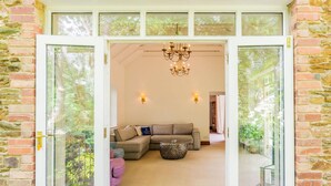 Ein modernes Interieur mit einer Eckcouch, einem Kronleuchter und Blick ins Grüne durch große Fenster.