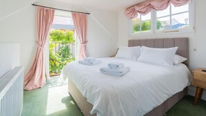 Ein Schlafzimmer mit einem großen Bett, weißer Bettwäsche, einem Holfnachtkästchen und Blick auf Grünfläche.