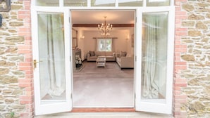 Ein Eingang mit Steinwänden und einer Glastür, die in ein Wohnzimmer mit einer Couch, einem Couchtisch und einer Kandelaber führt.