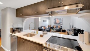 Une cuisine compacte dotée d’un îlot central, d’appareils électroménagers en acier inoxydable et de meubles de rangement en bois.