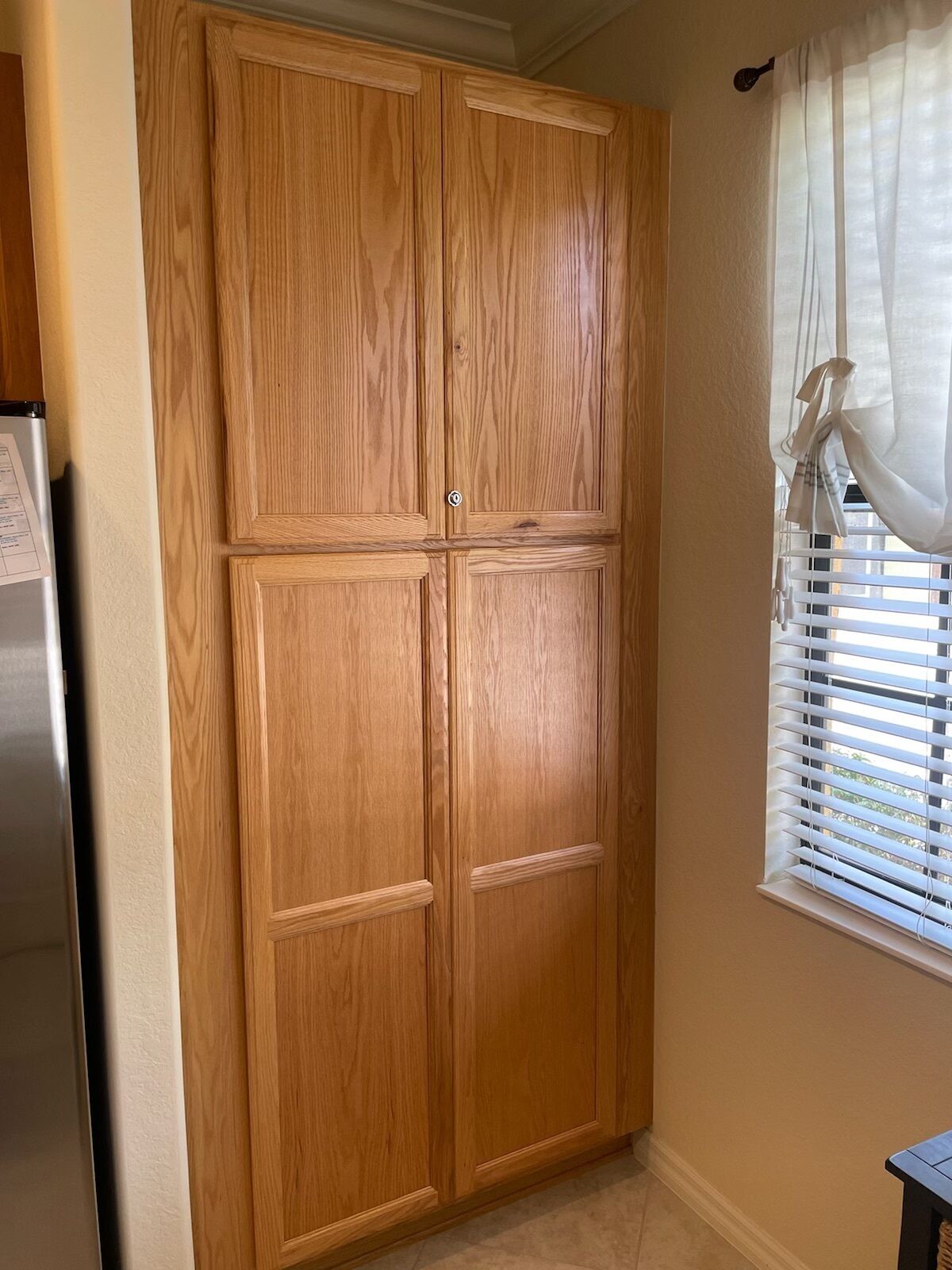 Un armario de madera con un tirador, una ventana con persianas y un refrigerador.