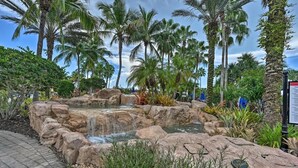 Un jardín tropical con una cascada, palmeras y un sendero pavimentado.