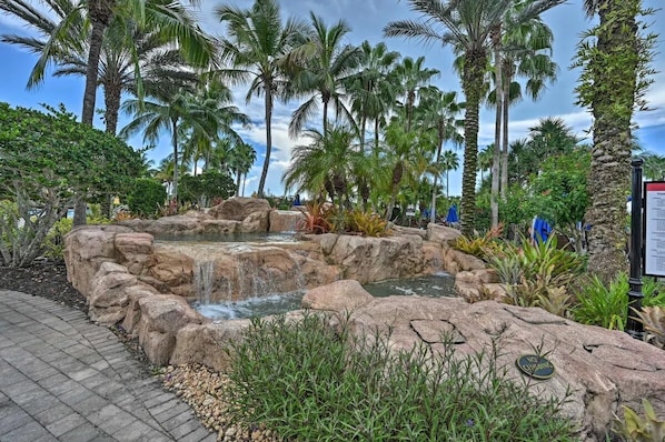 A tropical garden with a waterfall, palm trees, and a paved walkway.