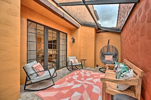A cozy patio area with a glass door leading to a room, a rocking chair, a wooden bench, and a patterned rug.