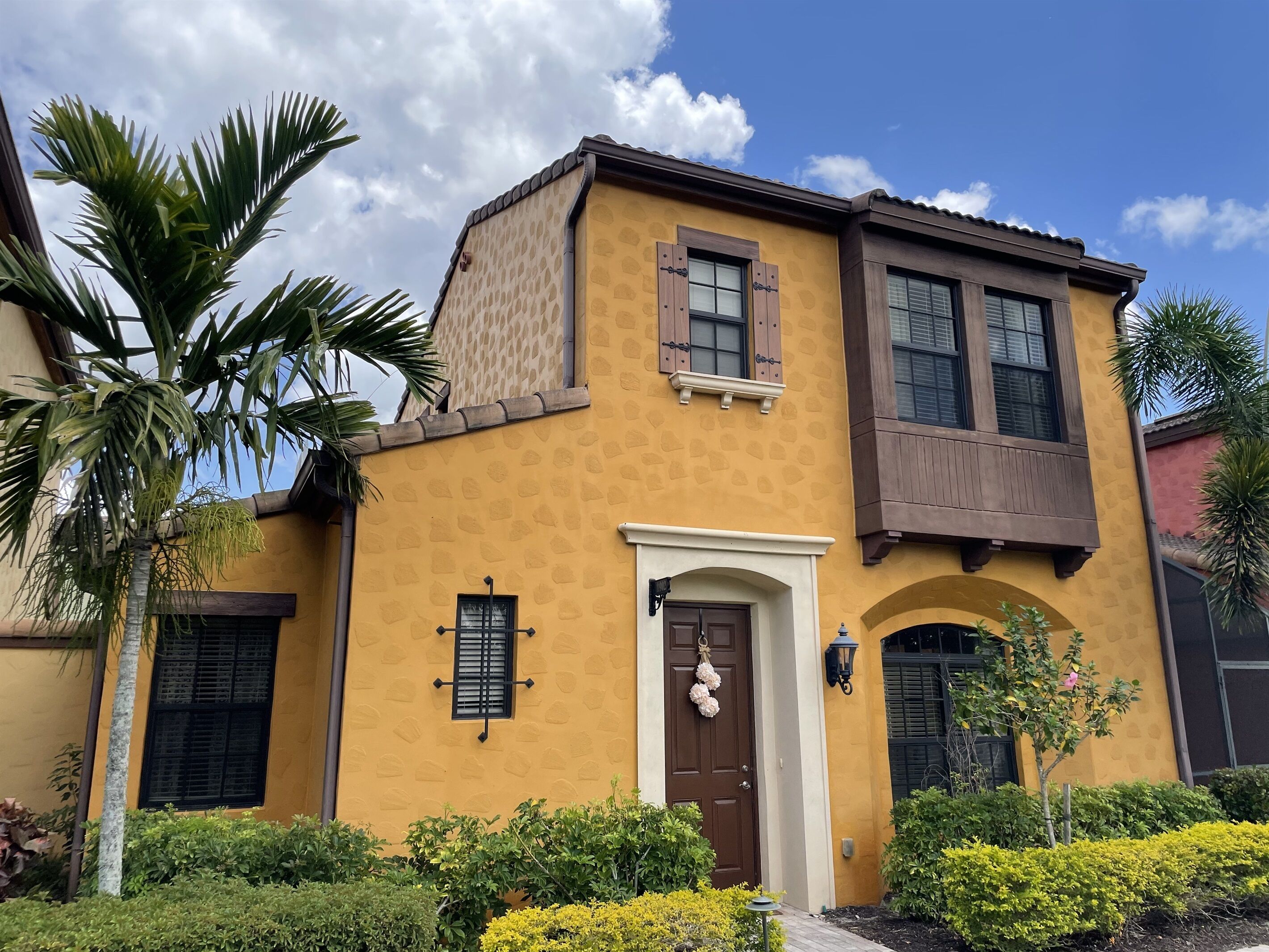 A two-story building with a yellow facade, brown shutters, and a small porch.