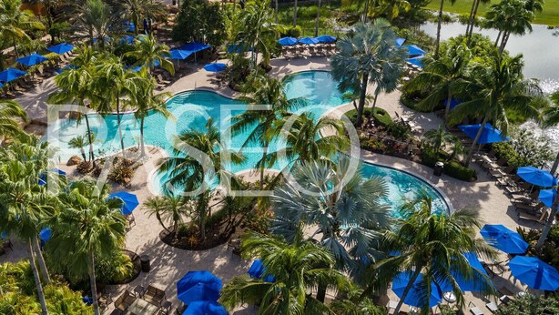 Un resort con varias piscinas rodeadas de palmeras y sombrillas azules.