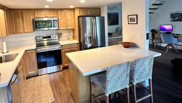 Una cocina moderna con electrodomésticos de acero inoxidable, armarios de madera y una isla central con taburetes de bar.