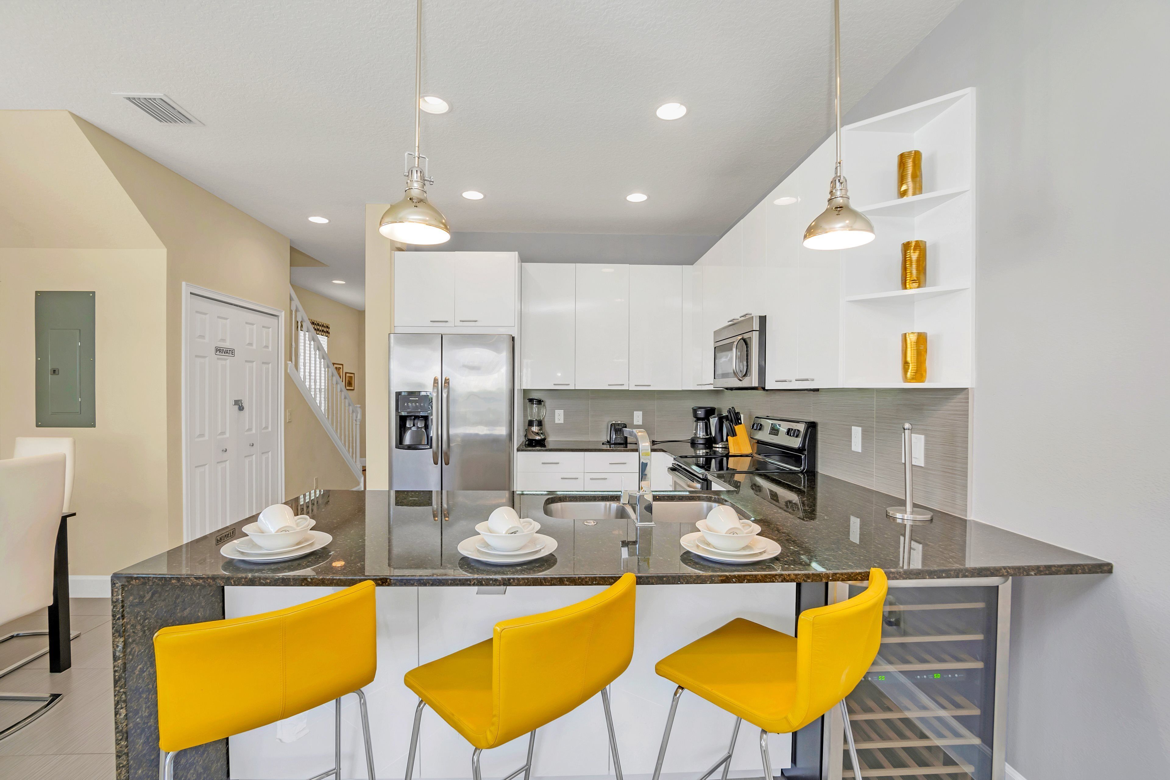 A modern kitchen with a central island, stainless steel appliances, and yellow bar stools.