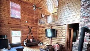 Interior acogedor de una cabaña de madera con chimenea, televisor y balcón.