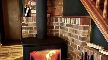 A wood-burning stove with a glass front, set in a corner with a brick wall and wooden staircase.