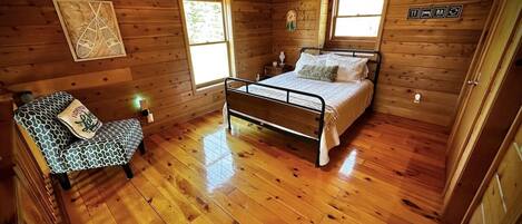 A wooden cabin room with a bed, a chair, and a ceiling fan.
