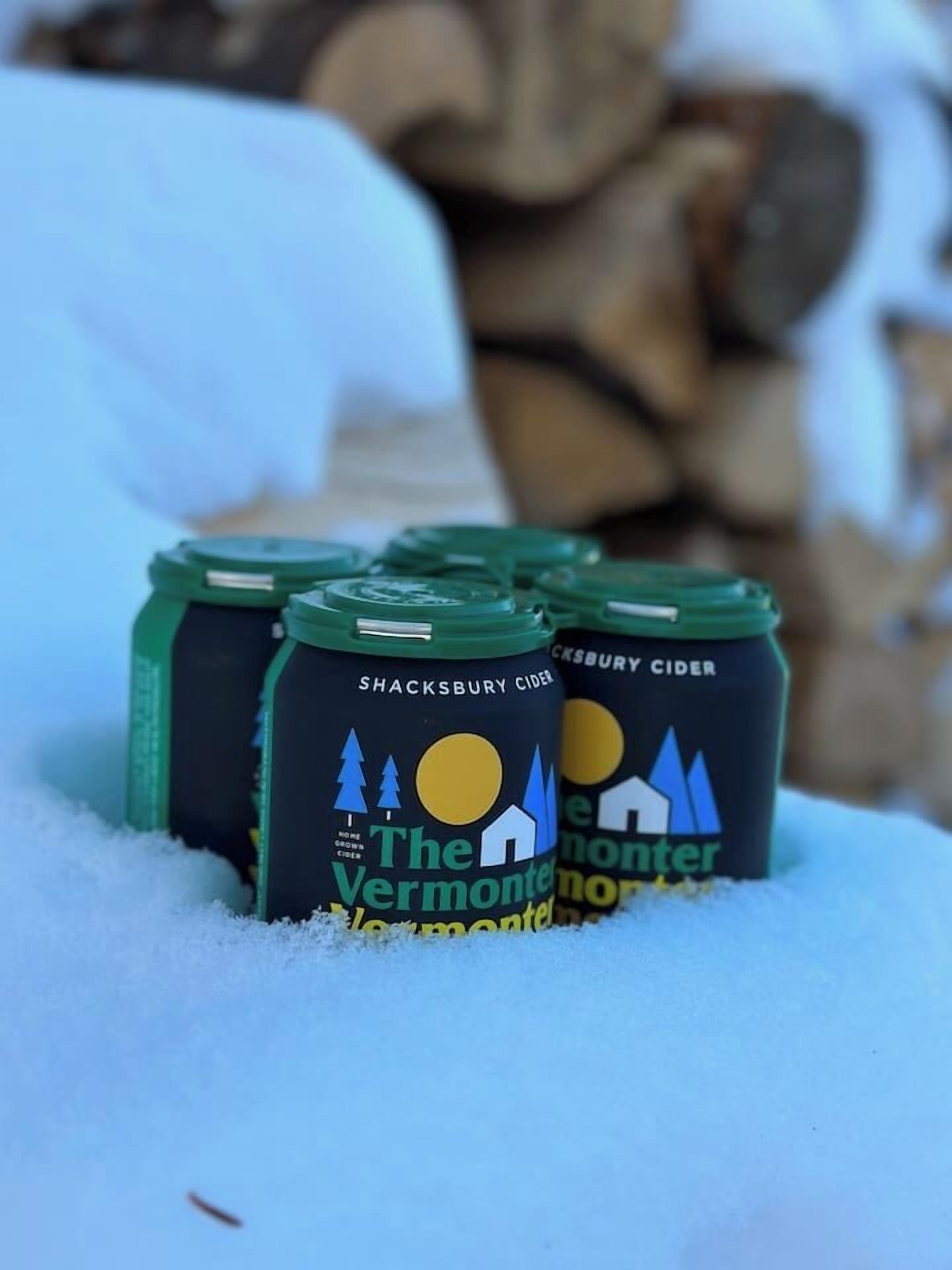 Cuatro botellas de Sidra Shacksbury con la etiqueta "The Vermont Monster" en un paisaje nevado.