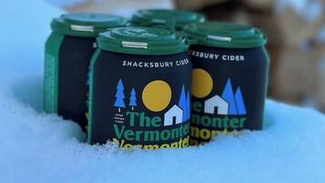 Cuatro botellas de Sidra Shacksbury con la etiqueta "The Vermont Monster" en un paisaje nevado.