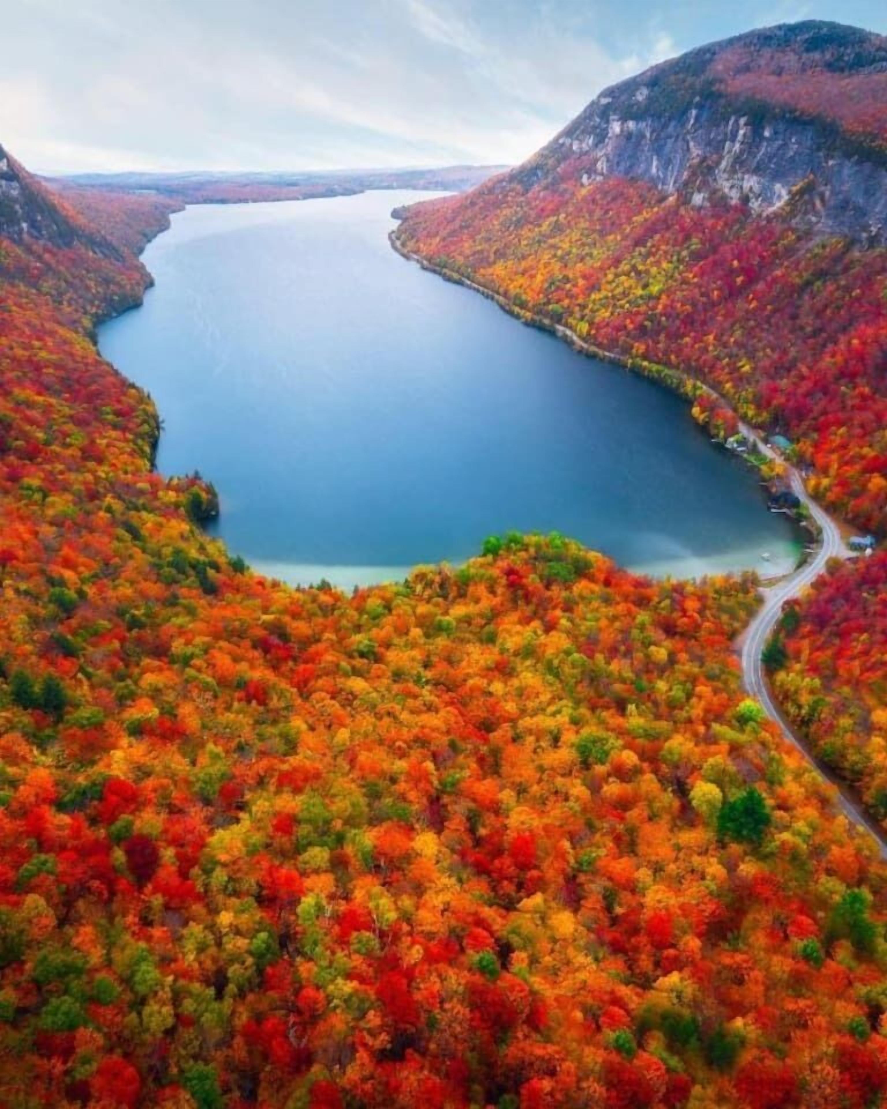 Un lac bordé d’arbres aux couleurs automnales et une route sinueuse.