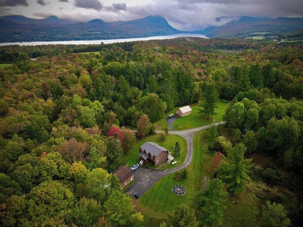 An aerial view of a rural property with a large house, a smaller building, and a driveway leading to a parking area. - HGTV Cabin Lake Willoughby/Burke/Jaypeak EV Chrgr (Barton)